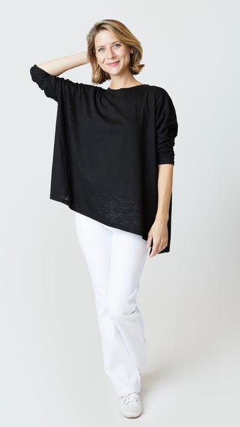 Model wearing black cotton tee with dropped shoulder 3/4 sleeve and side slits, white bootcut jeans, and white sneakers.
