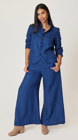 Model wearing indigo twill button front blazer jacket with rounded hem and standing collar, with indigo twill wide-leg pants.