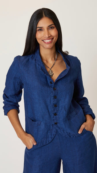 Model wearing indigo twill button front blazer jacket with rounded hem and standing collar, and short beaded necklace with pewter pendant.