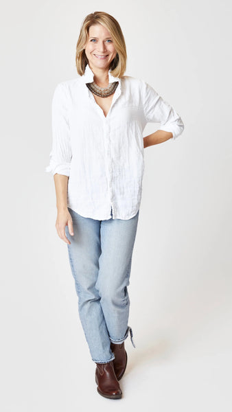 Model wearing white double cotton button-up shirt with beaded necklace, light-wash jeans, and brown leather boots. 