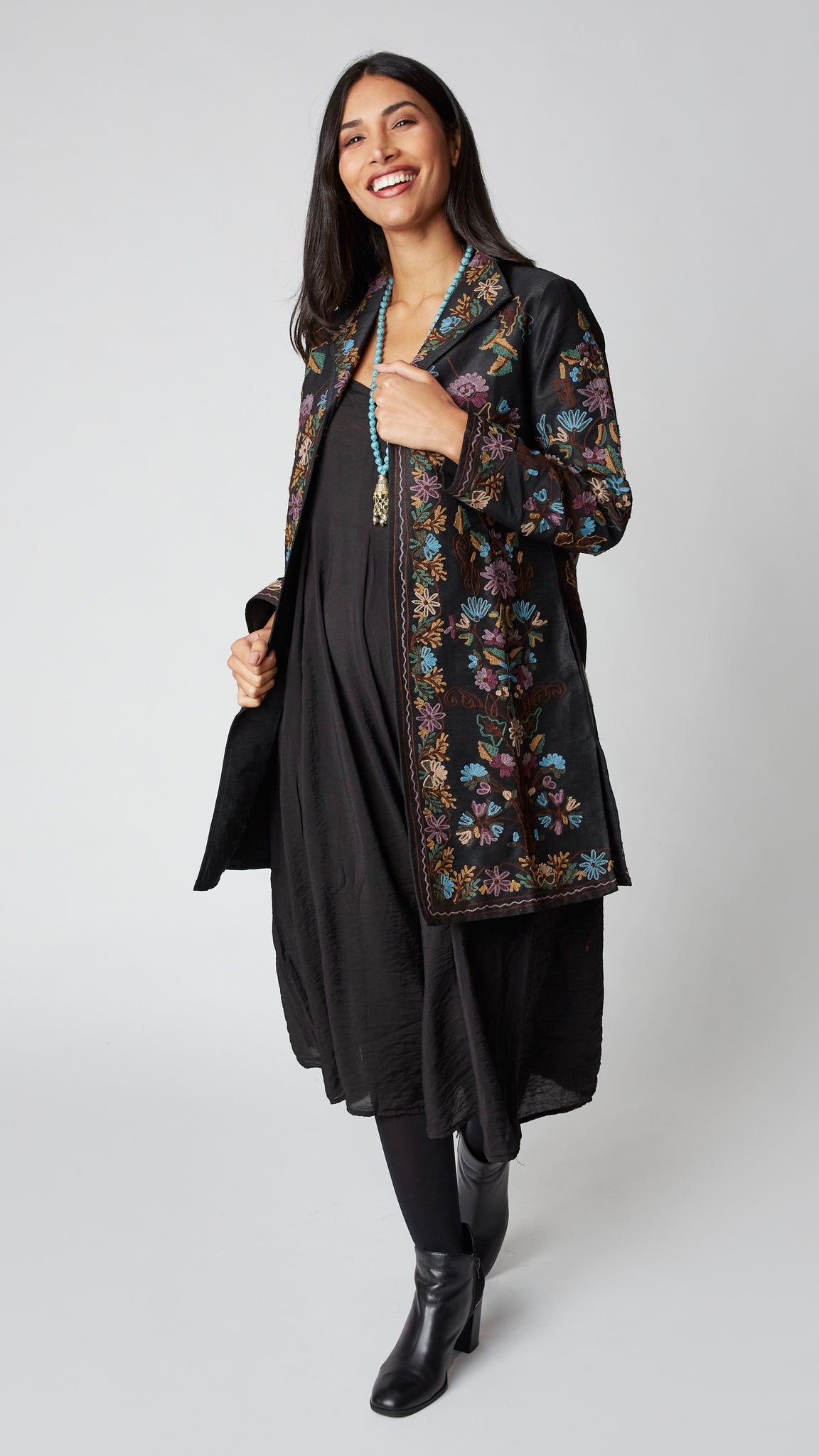 Model wearing black silk duster embroidered in dusty blue, purple, and brown tones over black rayon romper and black suede boots.
