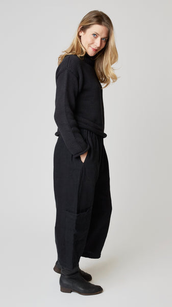 Model wearing black handknit cotton turtleneck sweater (slightly cropped), with black heavyweight linen cropped pant with side pockets above ankle darts, and black leather boots.