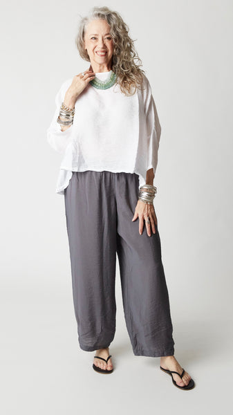 Model wearing cropped white rayon top with high round neckline, dropped shoulders and ¾ sleeves, gray cropped dart pants, silver bangles, and black flip-flops. 