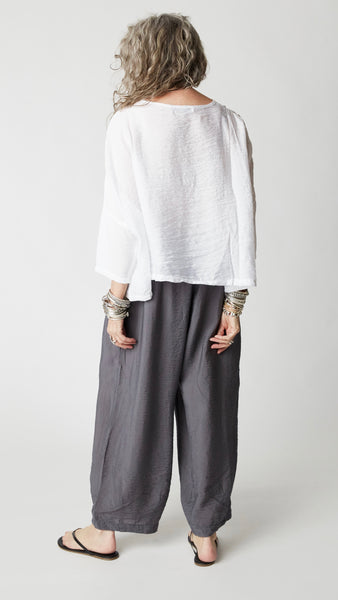 Model wearing cropped white rayon top with high round neckline, dropped shoulders and ¾ sleeves, gray cropped dart pants, silver bangles, and black flip-flops.