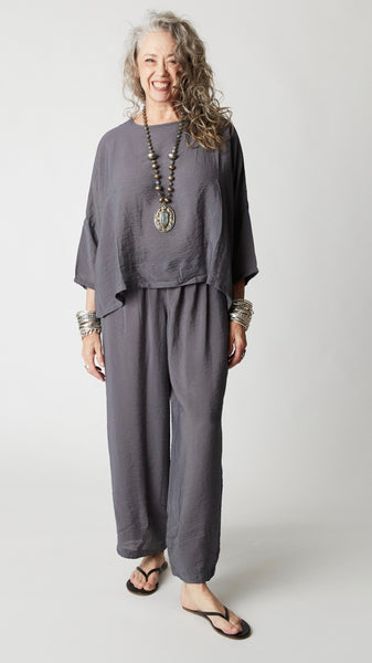 Model wearing gray rayon cropped dart pant, gray rayon dropped shoulder cropped top, silver bangles and beaded pendant necklace, and black flip-flops.