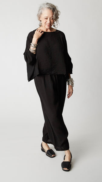 Model wearing black rayon cropped dart pant, cropped rayon top with dropped shoulder and 3/4 sleeves, silver bangles, and black open-toed flats. 