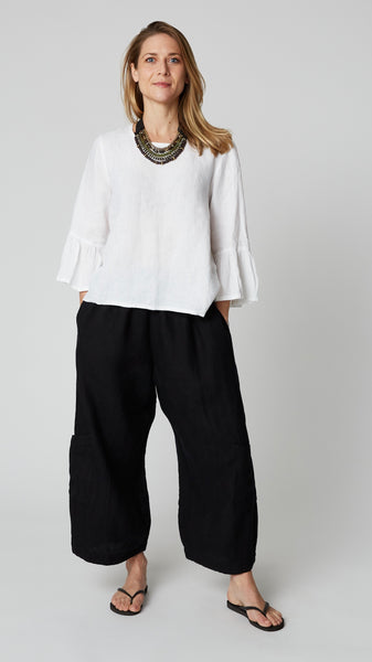 Model wearing black linen cropped pant with side pockets, white high-low top with 3/4 ruffle sleeve, and black flip-flops.