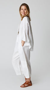 Model wearing white linen cropped pant with side pockets, white high-low top with 3/4 ruffle sleeve, and brown leather sandals.