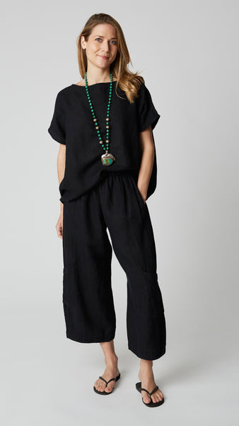 Model wearing black linen cropped pant with side pockets, black boxy cap-sleeve top, turquoise necklace,  and black flip-flops.