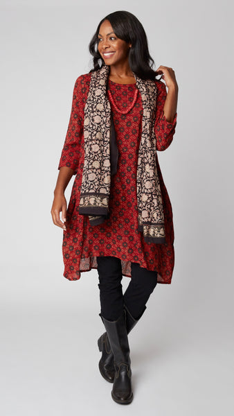 Model wearing "shadow dot rust" block print tunic dress with 3/4 sleeves, high-low hemline and bubble silhouette, with beaded necklace, block print scarf, and black leather boots.