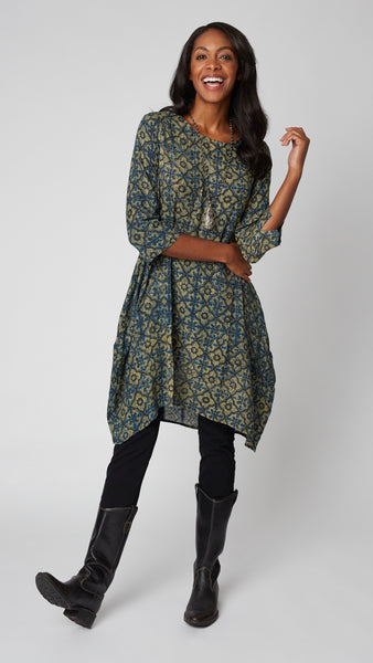 Model wearing "ochre" block print tunic dress with 3/4 sleeves, high-low hemline and bubble silhouette, with long beaded necklace, and black leather boots.