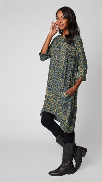 Model wearing "ochre" block print tunic dress with 3/4 sleeves, high-low hemline and bubble silhouette, with long beaded necklace, and black leather boots.
